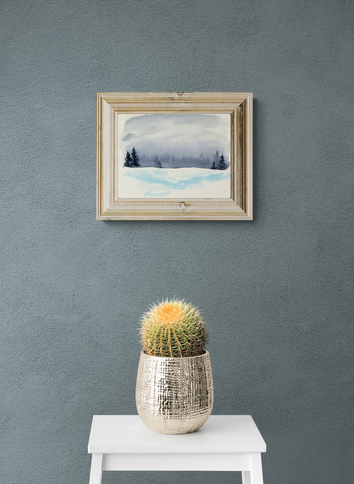 Framed artwork on a gray wall with a cactus in a pot below.
