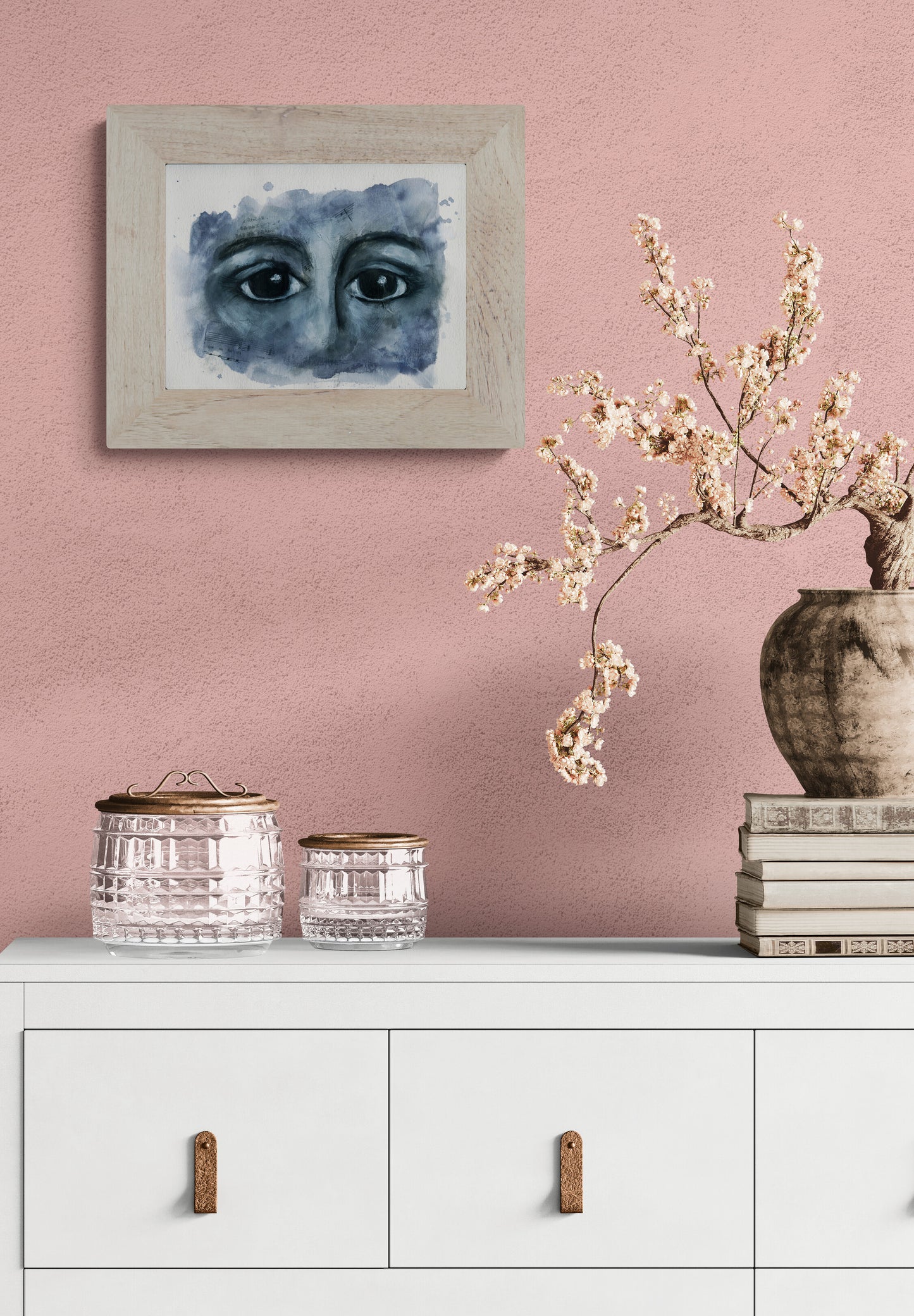 Framed artwork on a pink wall above a white cabinet with decorative items.