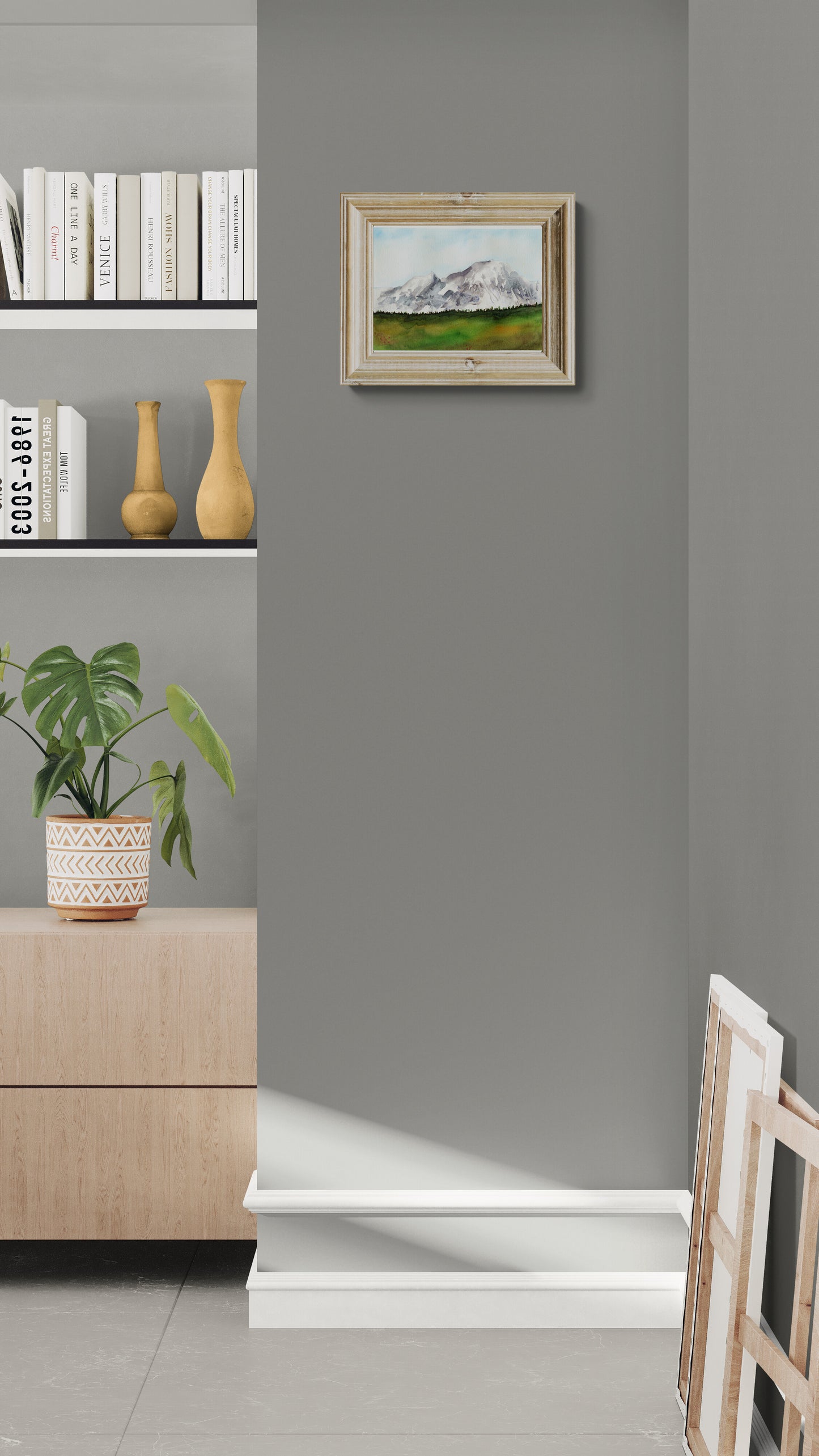 Framed artwork on a gray wall with a shelf and plant in the foreground