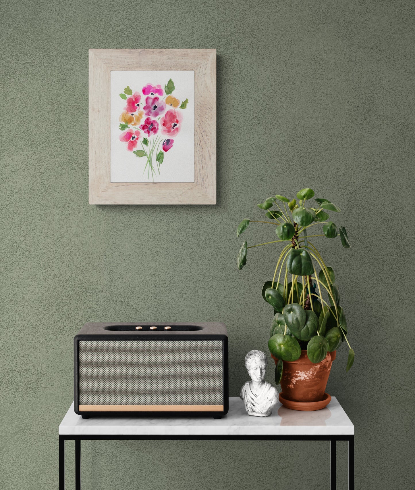 Framed floral artwork on a green wall above a table with a radio and decorative items.