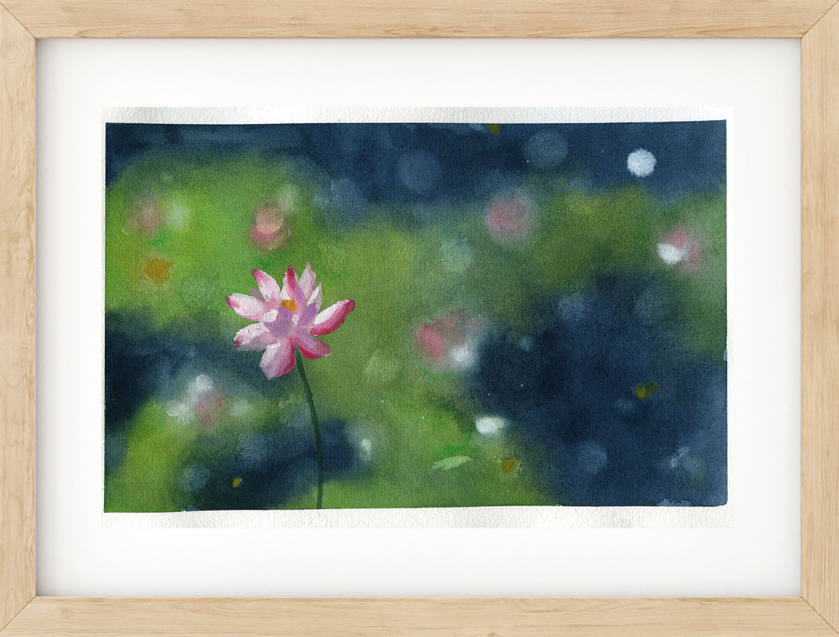 A framed watercolor painting of a single pink lotus flower on a dark blue and green background, presented in a light wood frame with a white mat.