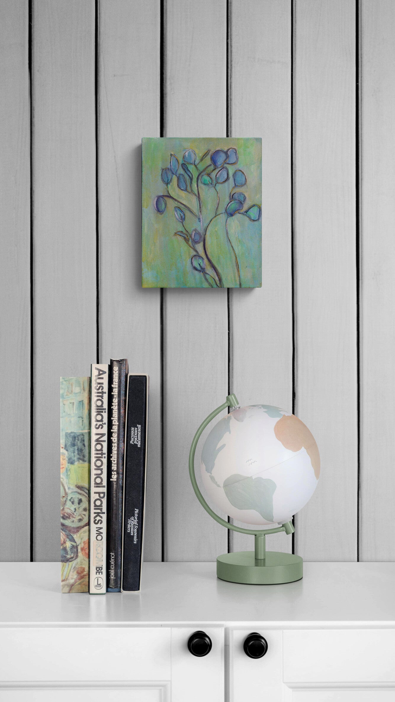 Small painting, books, and globe on a white surface with a gray paneled background.