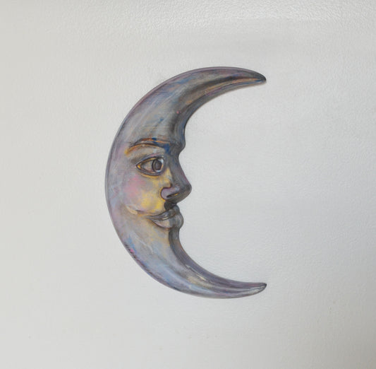 Decorative moon-shaped object with a face on a light gray background