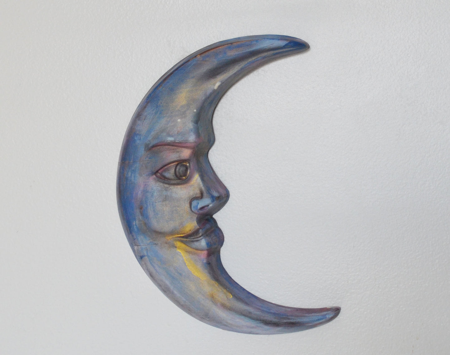 Decorative wall art in the shape of a half moon with a face on a light gray background