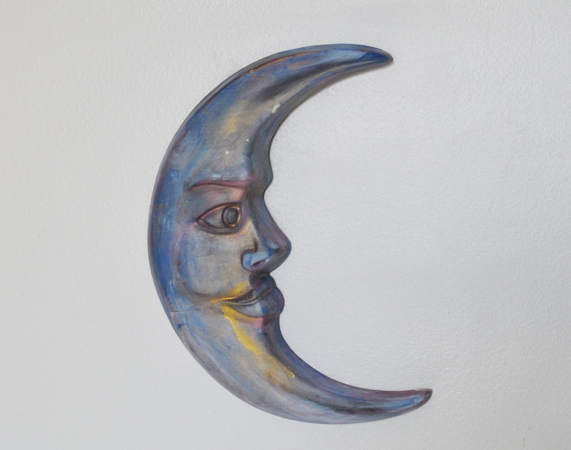 Decorative wall art in the shape of a half moon with a face on a light gray background
