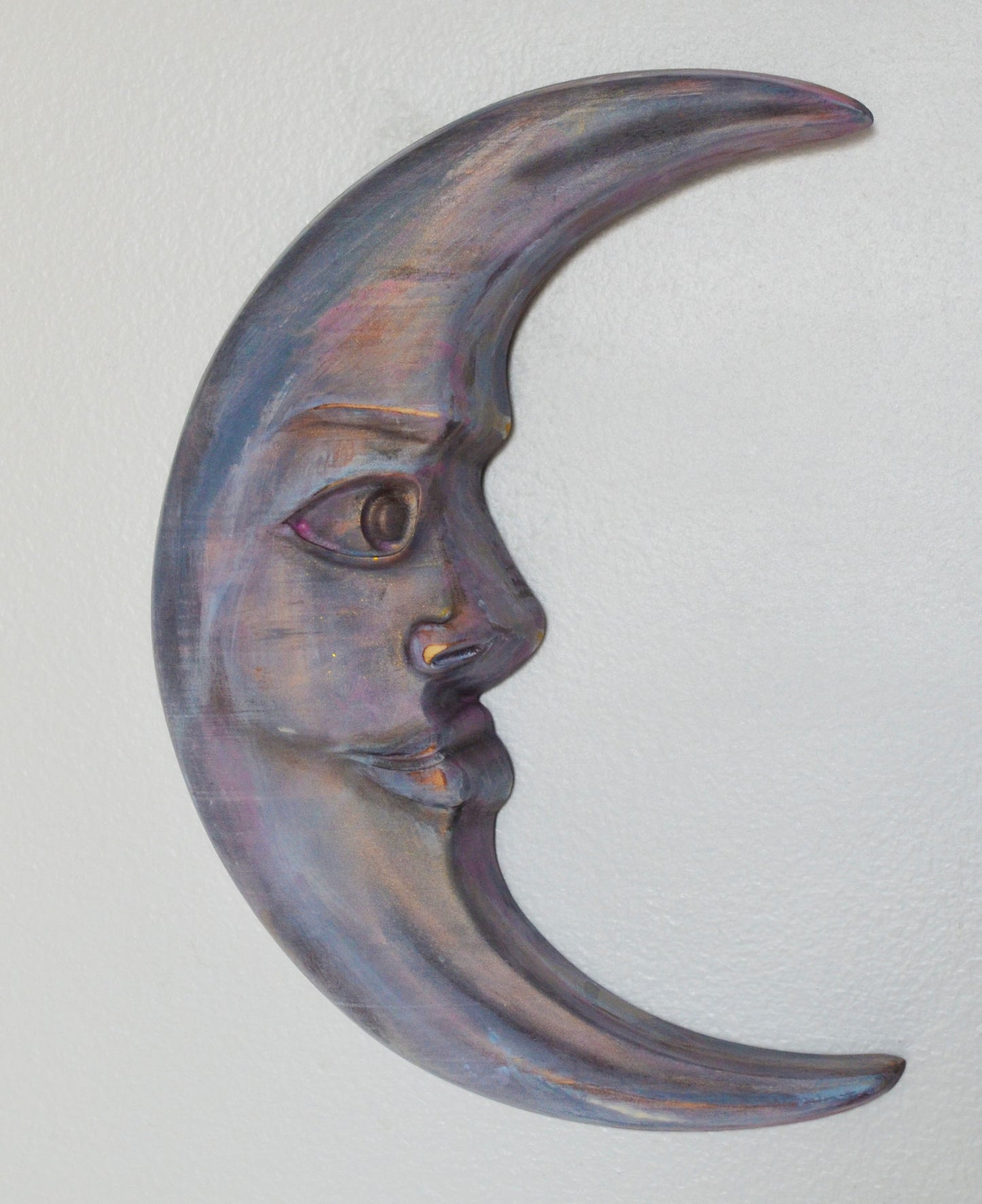 Decorative wall art in the shape of a crescent moon with a face on a light gray background