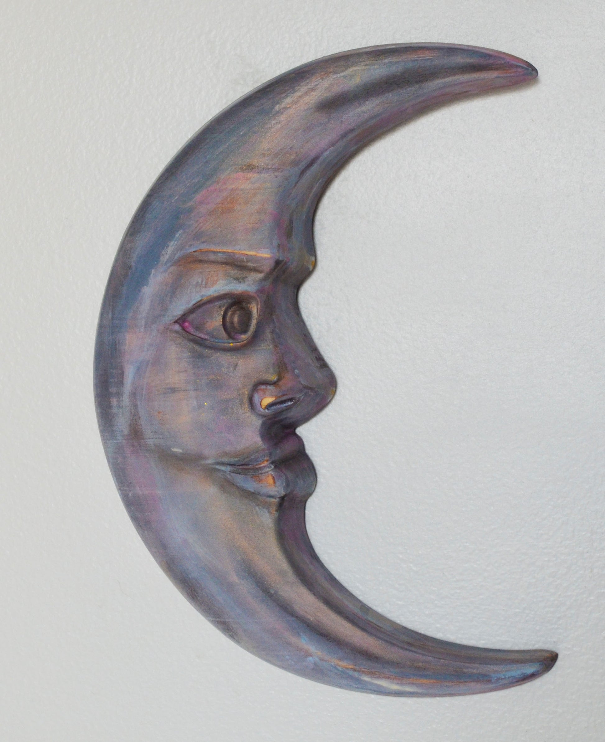 Decorative wall art in the shape of a crescent moon with a face on a light gray background