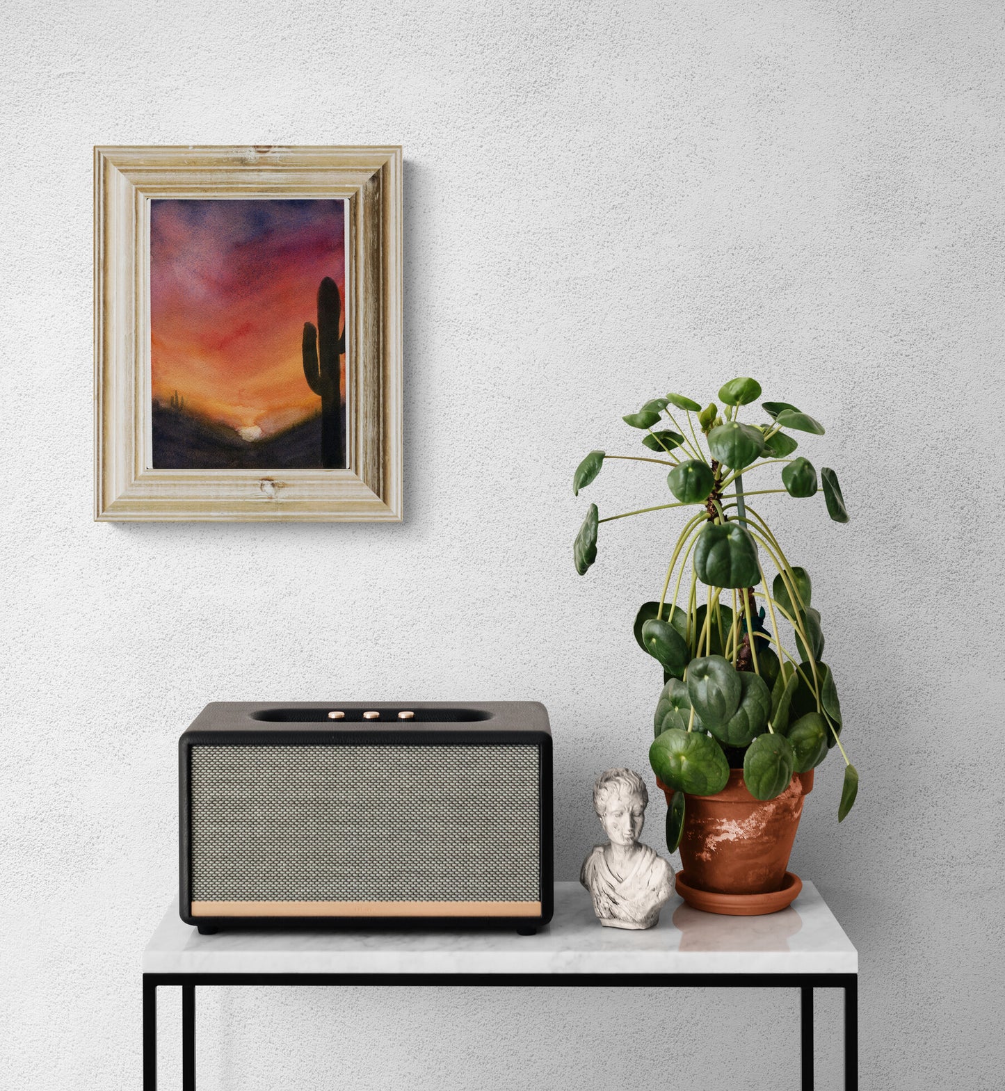 Modern radio on a white table with a framed artwork, plant, and small sculpture against a light gray wall.