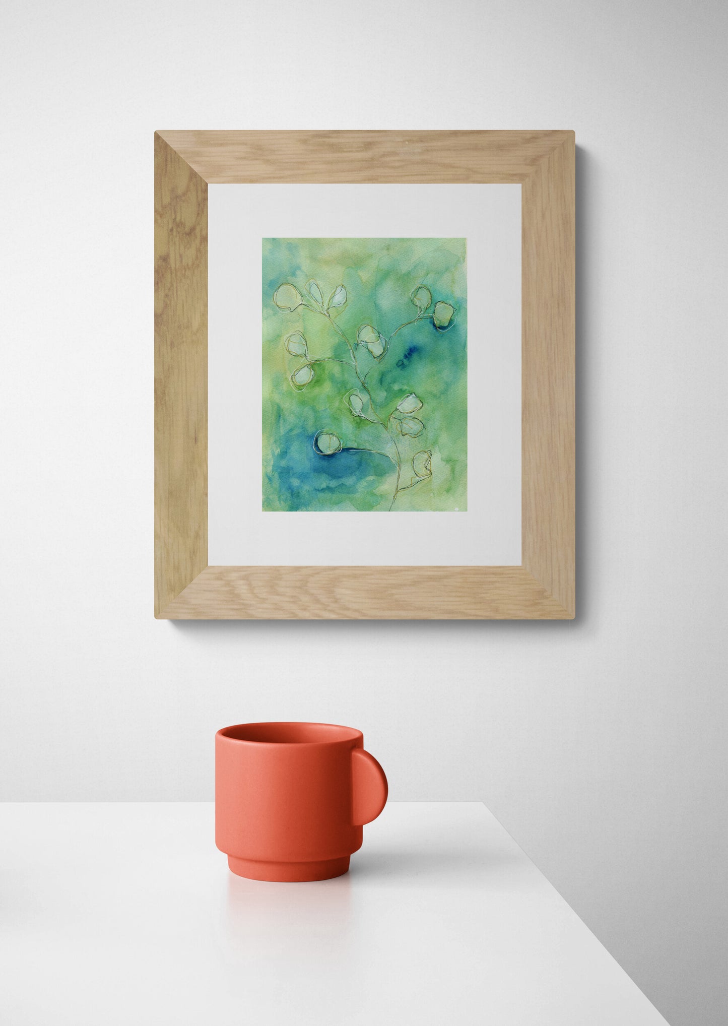 Framed artwork with a watercolor design on a white wall above a red mug.