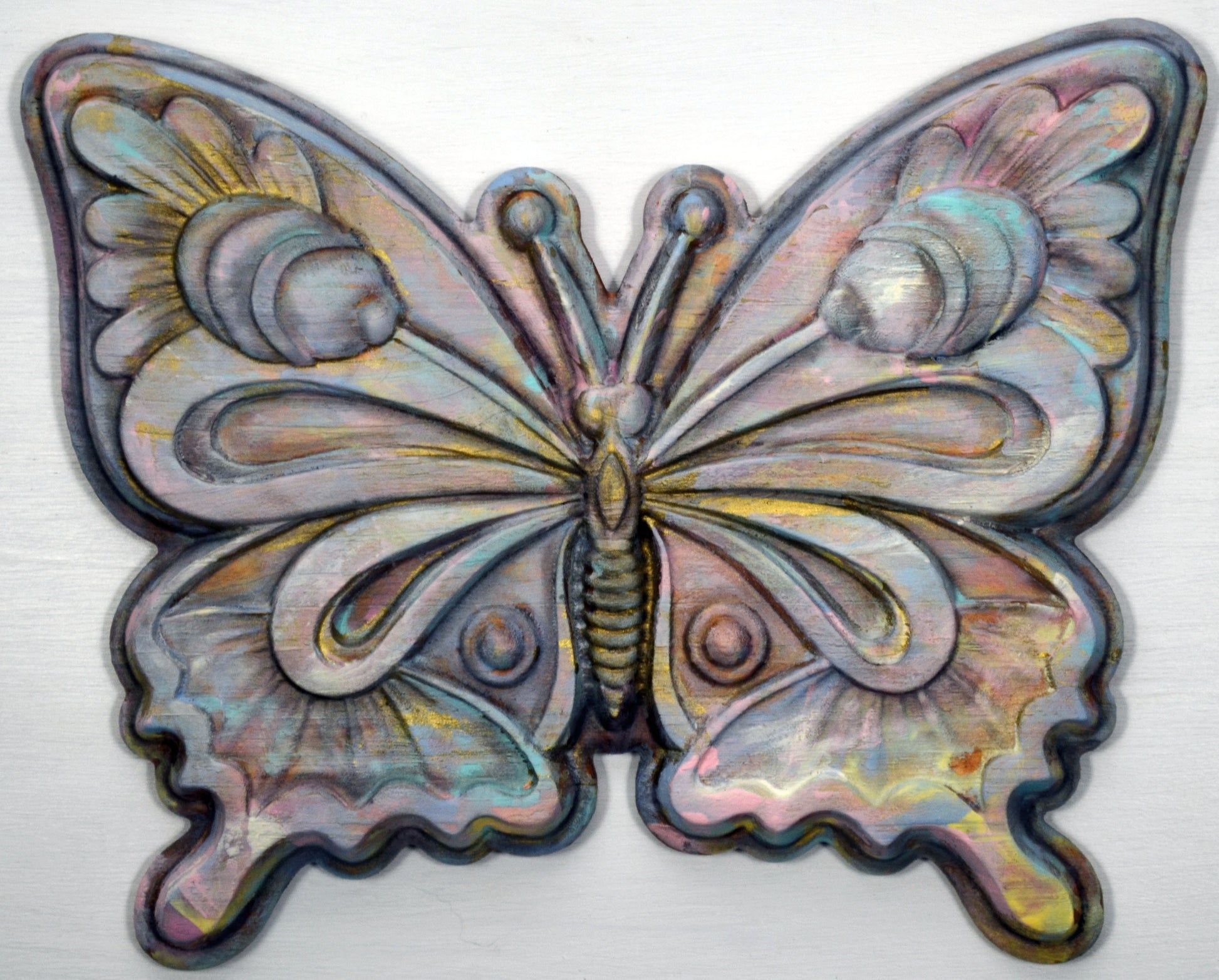 A hand-painted 3D wood carving of a multicolored butterfly with a wax finish.