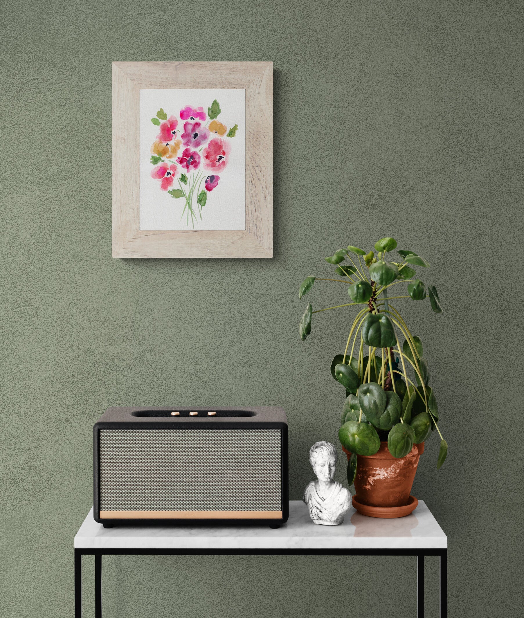 Framed floral artwork on a green wall above a table with a radio and decorative items.