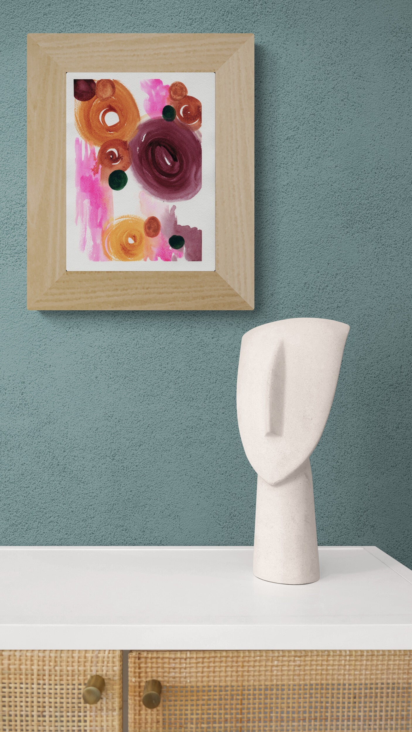 White ceramic head sculpture on a white surface with a framed abstract art piece on a blue wall.