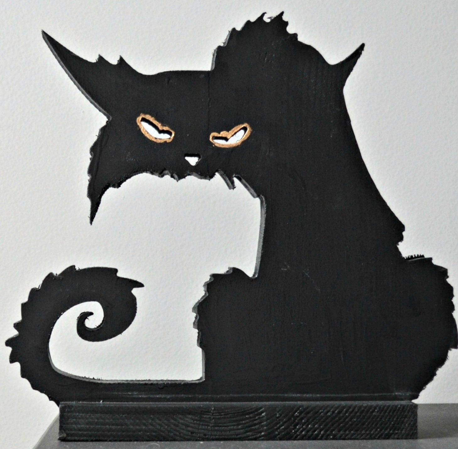 A 3D wood carving of a black cat with a spooky expression, featuring a dark body and orange eyes, intended for Halloween decoration.