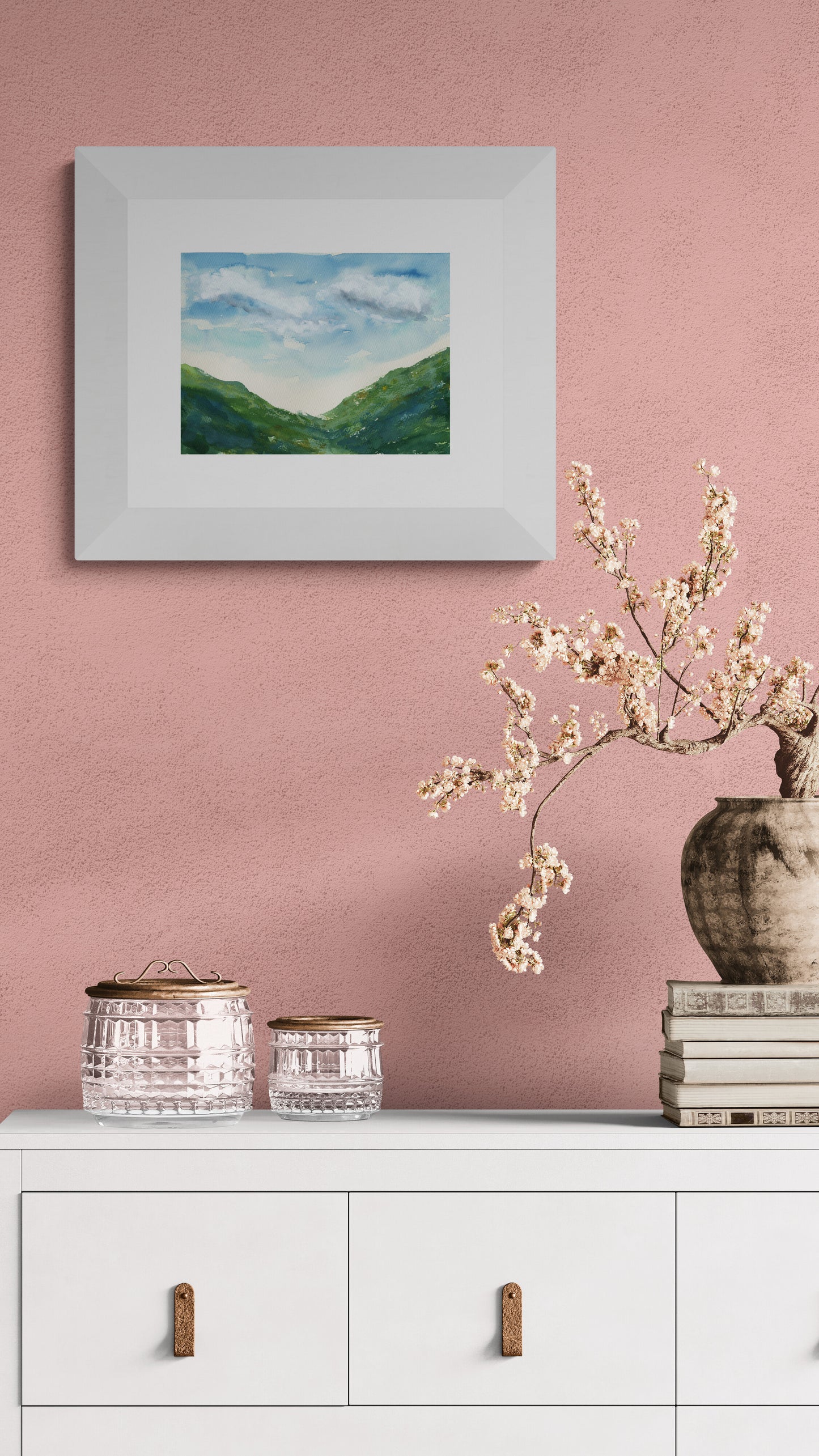 Framed landscape painting on a pink wall with decorative items below.
