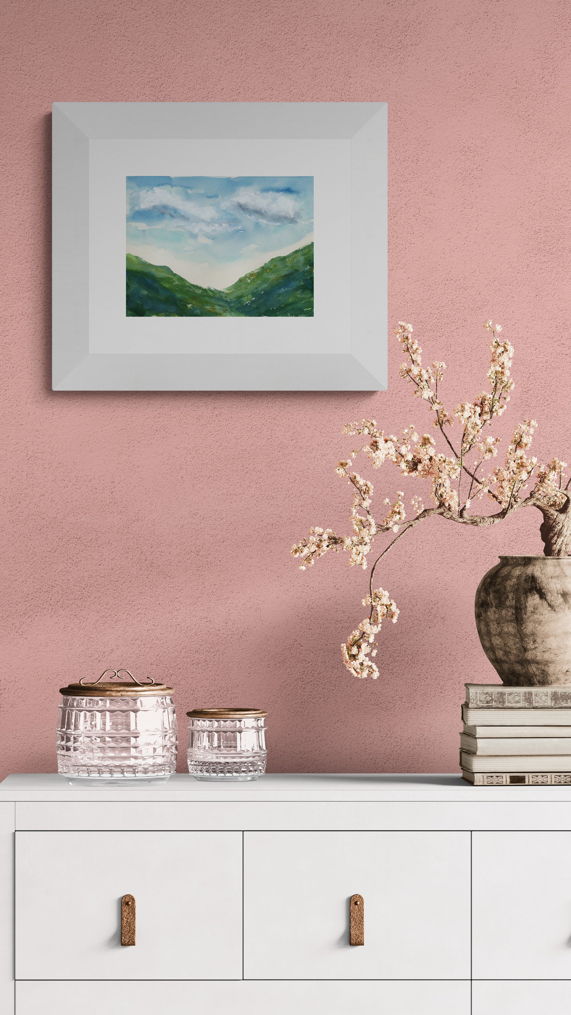 Framed landscape painting on a pink wall with decorative items below.