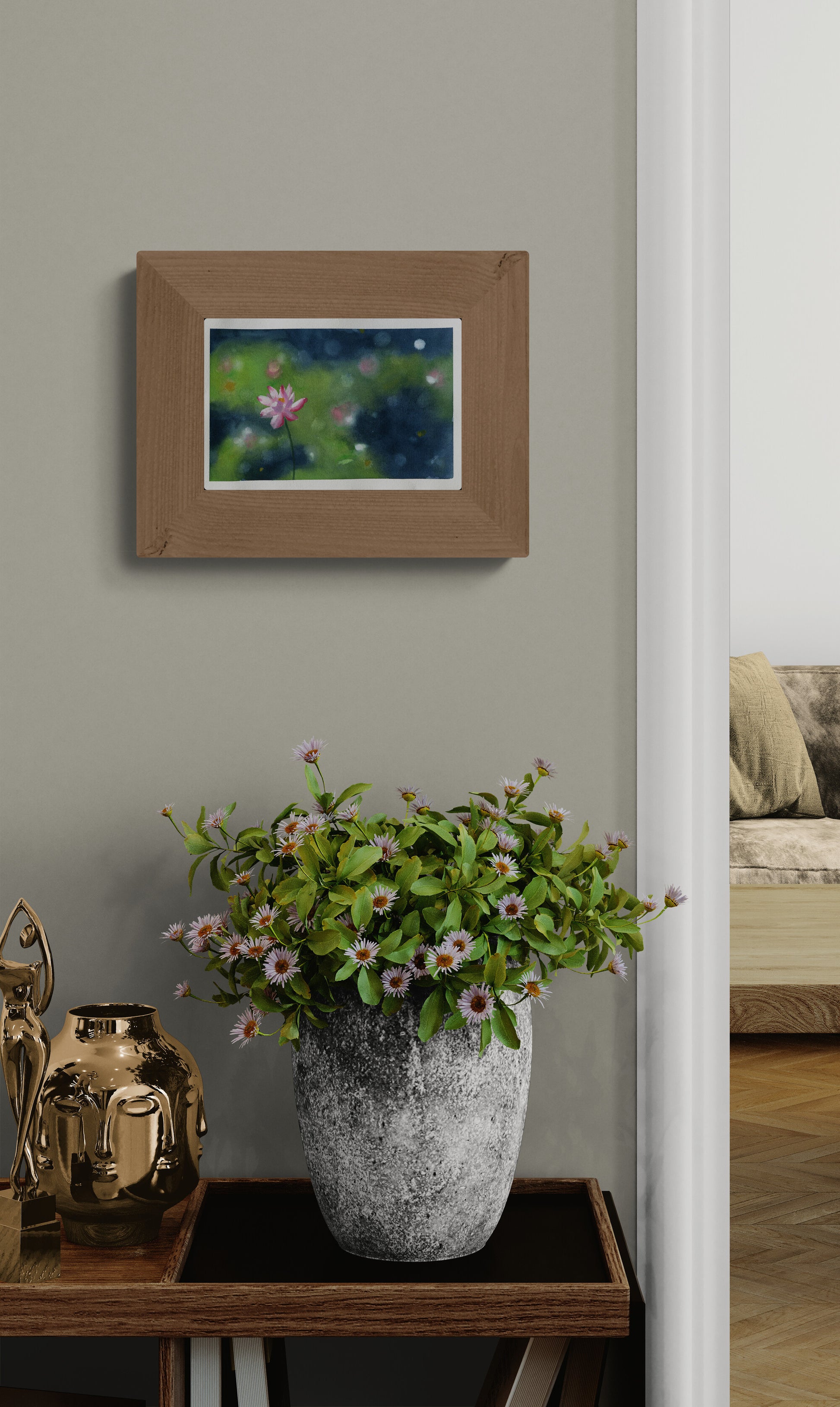 A framed art print depicting a pond scene with green lily pads and pink flowers, styled on a wall above a potted plant on a wooden console table.