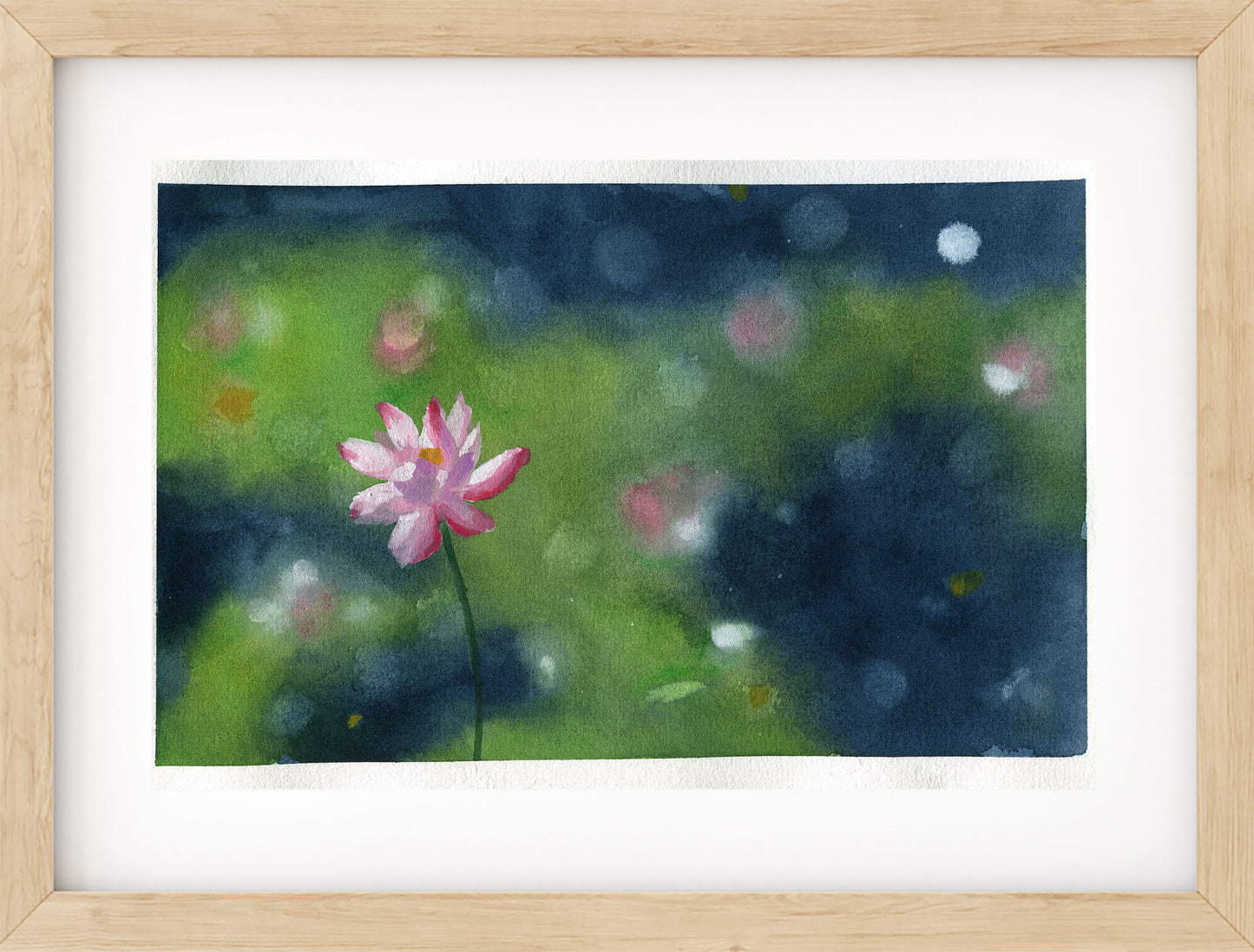 A framed watercolor painting of a single pink lotus flower on a dark blue and green background, presented in a light wood frame with a white mat.