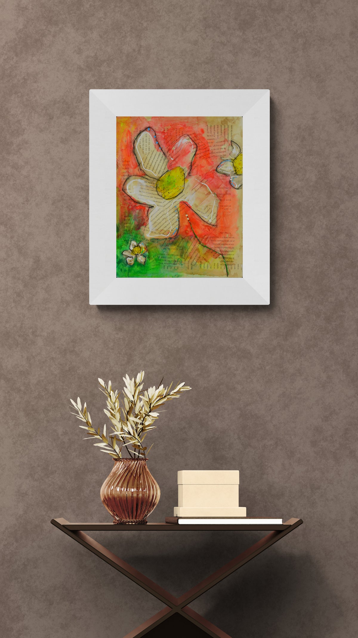 A framed abstract floral painting with white, red, green, and yellow tones hangs on a textured brown wall above a small table with a vase and books.
