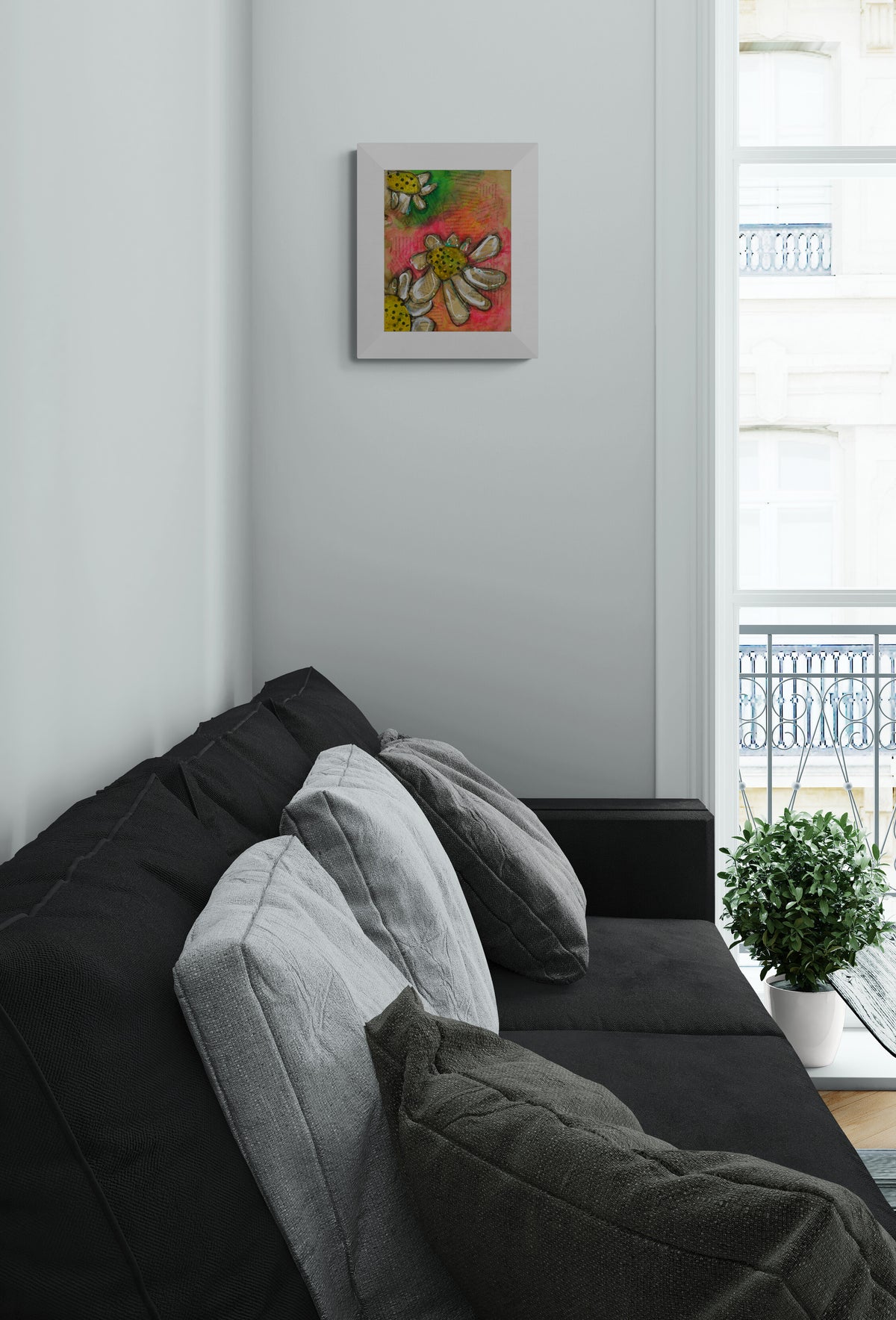 A framed abstract floral art print hangs on a light gray wall above a dark gray sofa with gray and charcoal pillows in a modern living room setting.