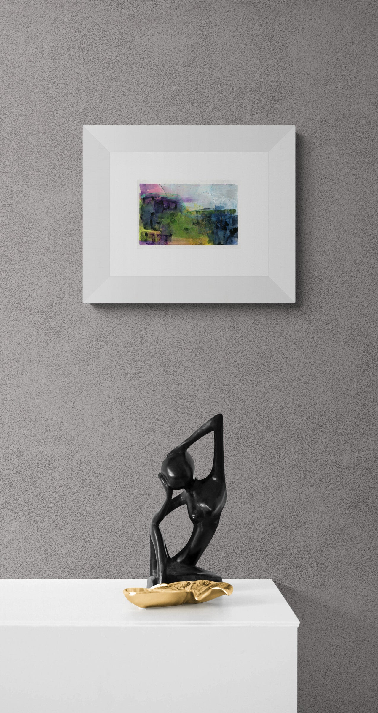 Framed abstract painting on a gray wall with a black sculpture and gold object below.
