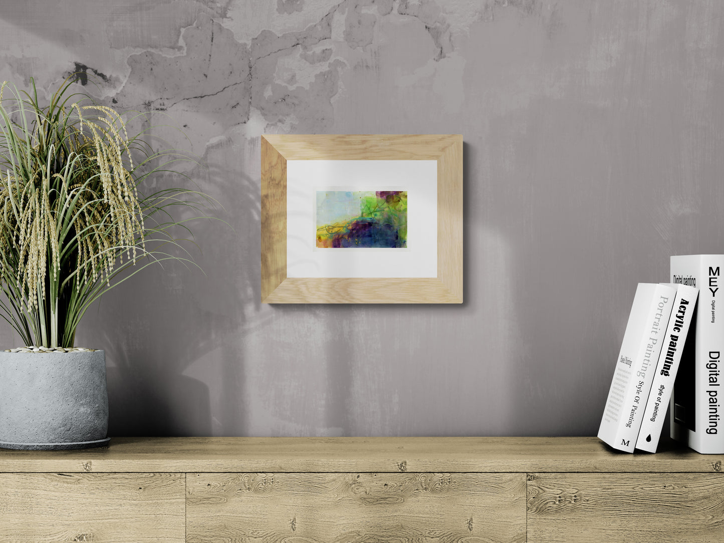 Framed artwork on a gray wall with books and a plant below