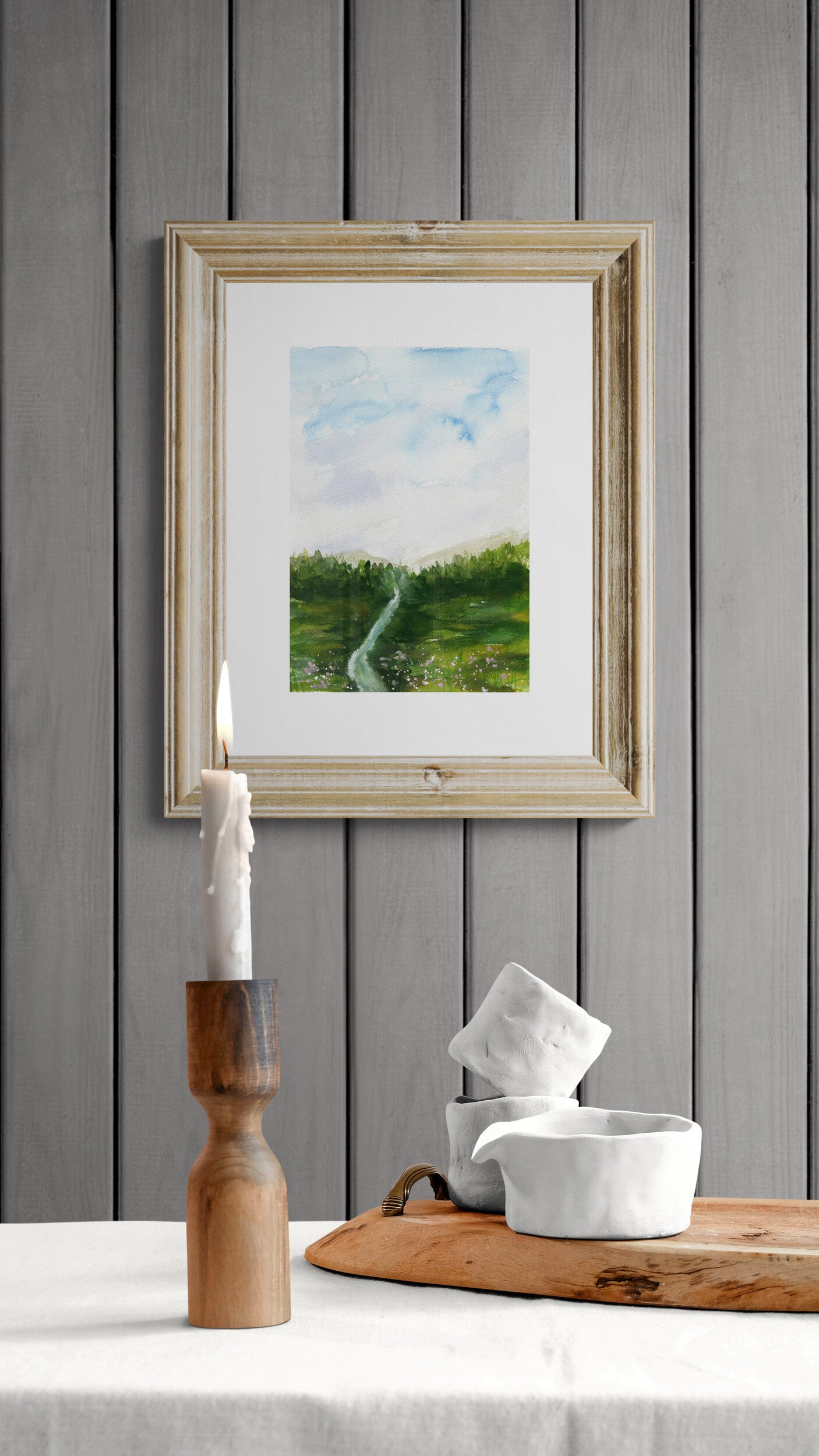 Framed landscape painting on a gray wall with a wooden table and decorative items.