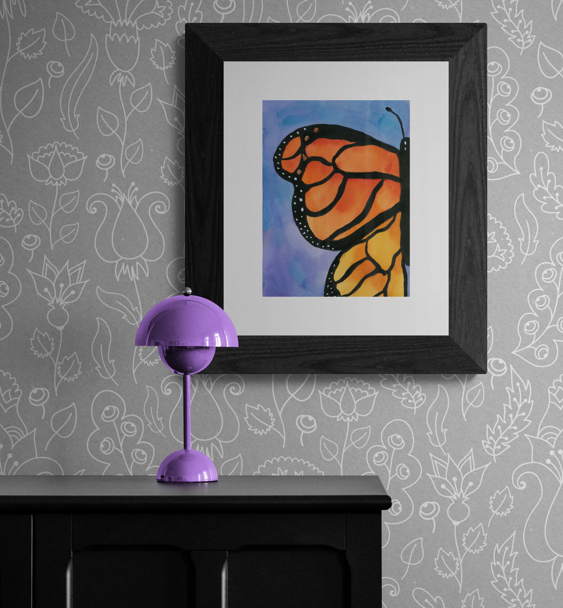 Framed artwork of a butterfly on a wall with a purple lamp below.