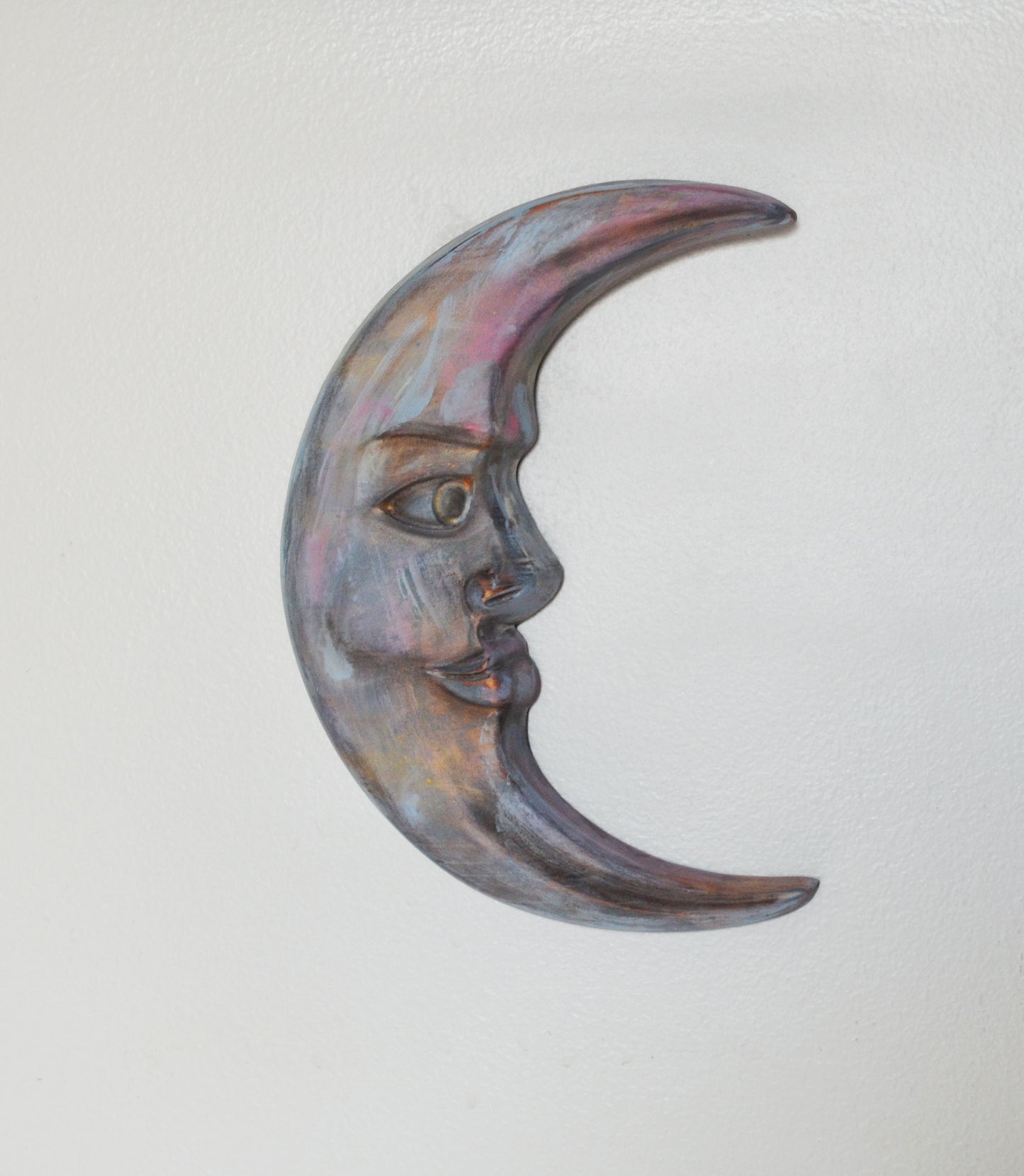 Decorative wall art in the shape of a crescent moon with a face on a light gray background