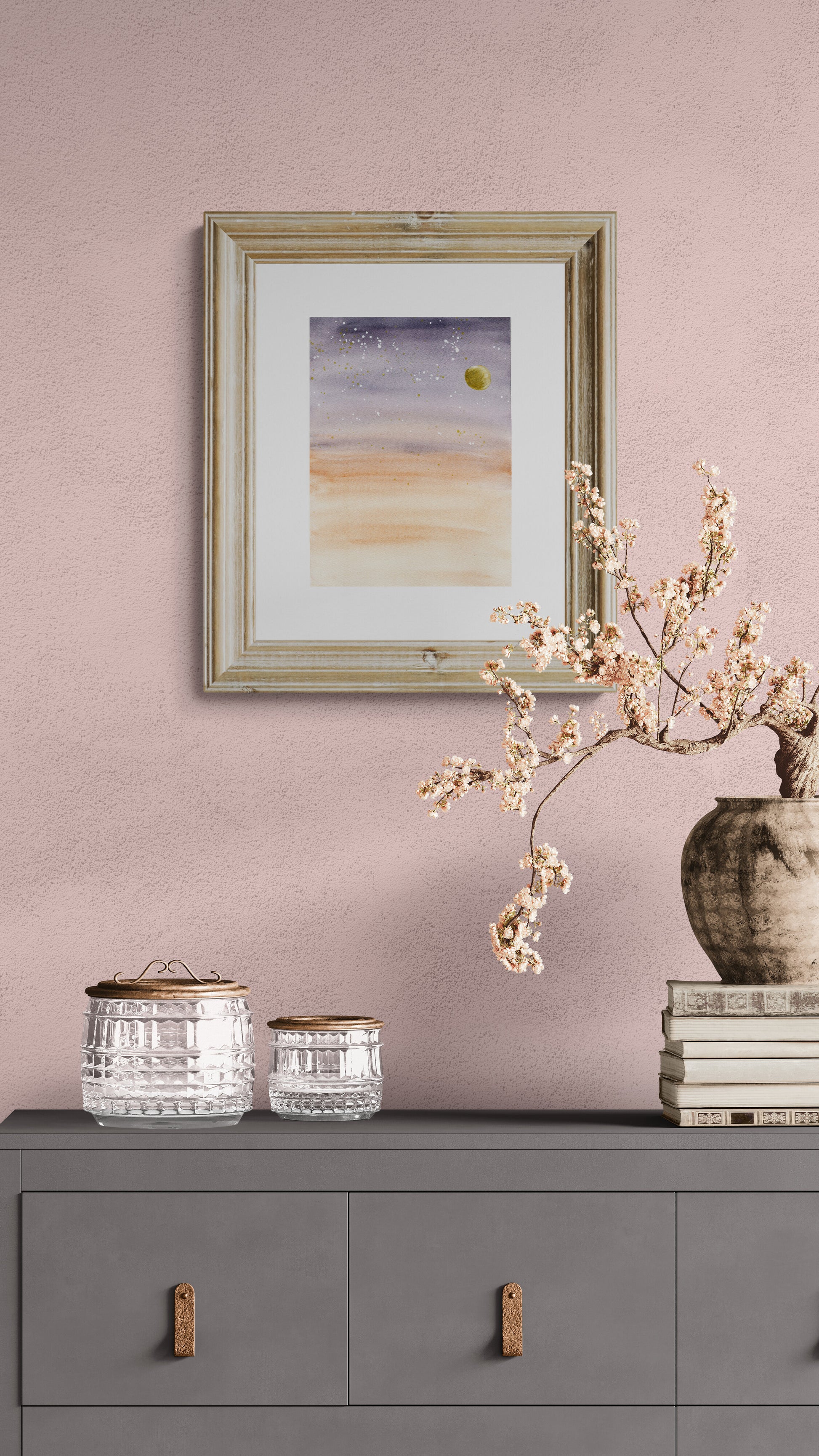 Framed artwork on a pink wall above a gray cabinet with decorative items.