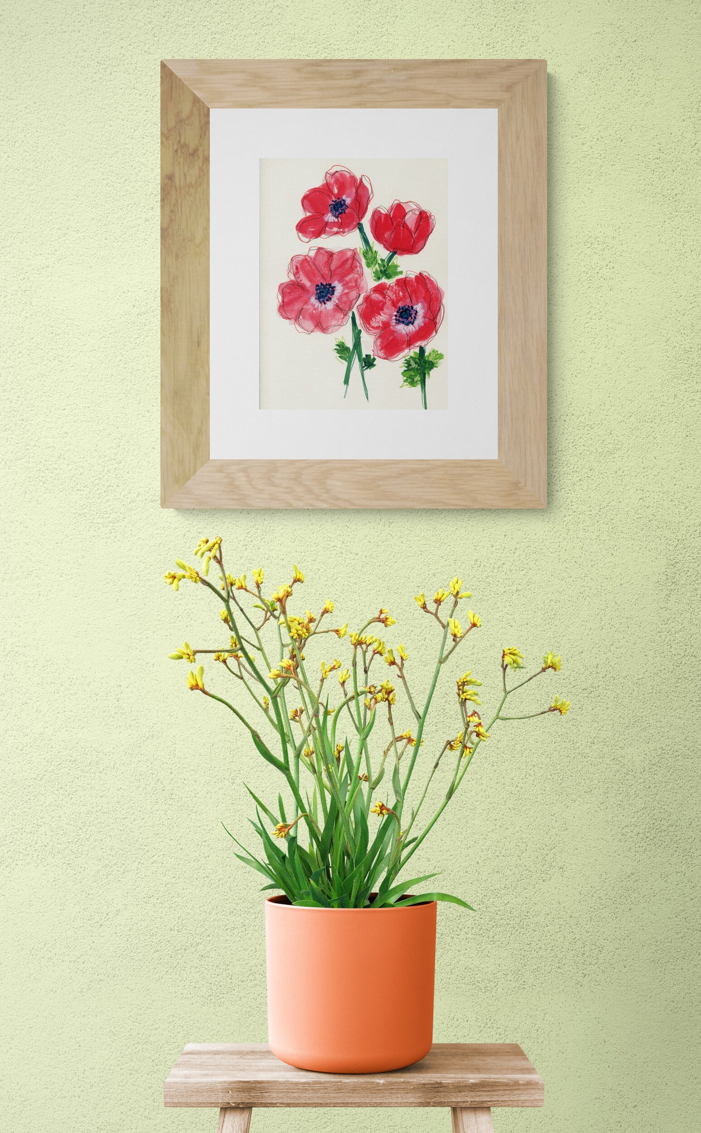 Framed artwork of flowers on a wall with a potted plant below.