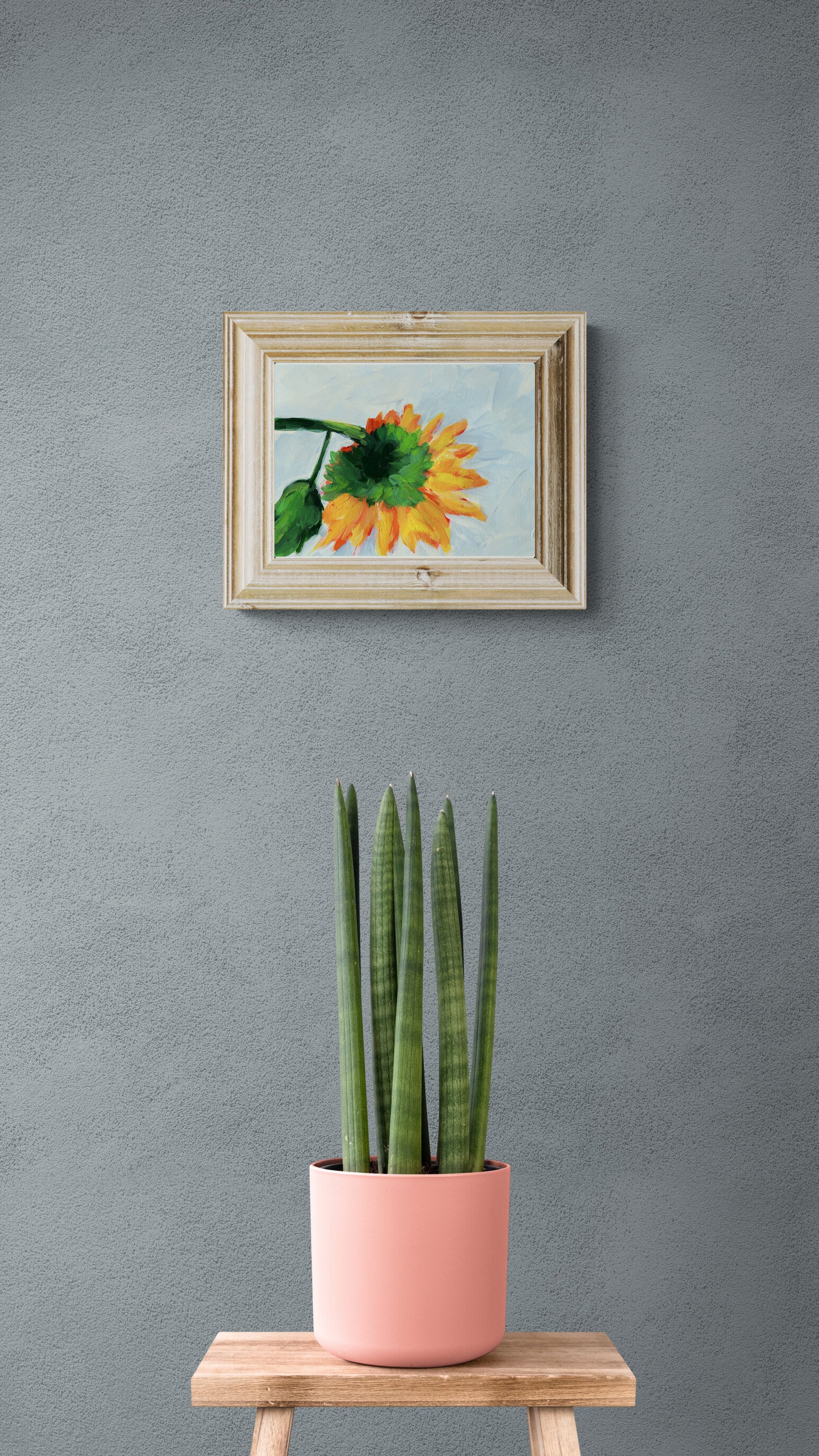 Framed artwork of a sunflower on a gray wall with a potted plant in the foreground.
